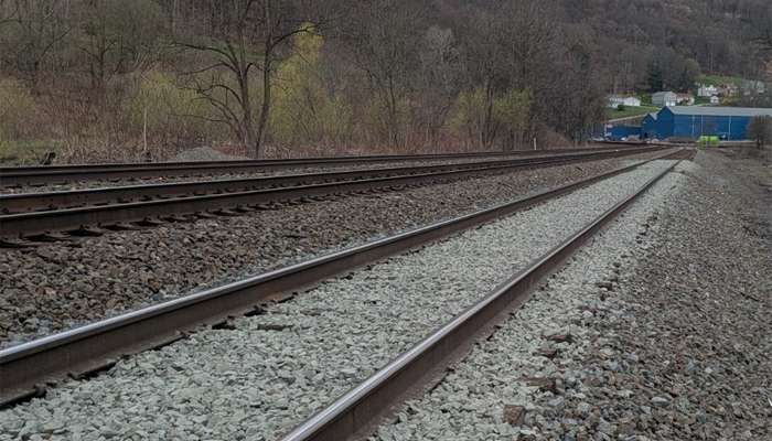 Newly constructed railroad track with fresh stone ballast alongside an existing track in a rural Pennsylvania corridor.